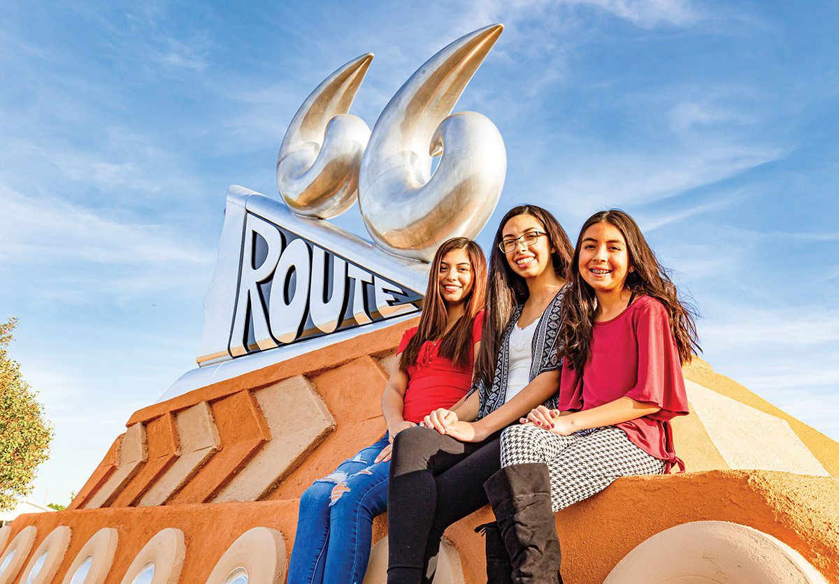 Three girls sit at the Route 66 Monument